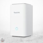 Reolink WLAN-Router in Weiß mit blauer LED-Anzeige auf einer hellen Oberfläche mit grauem Hintergrund.